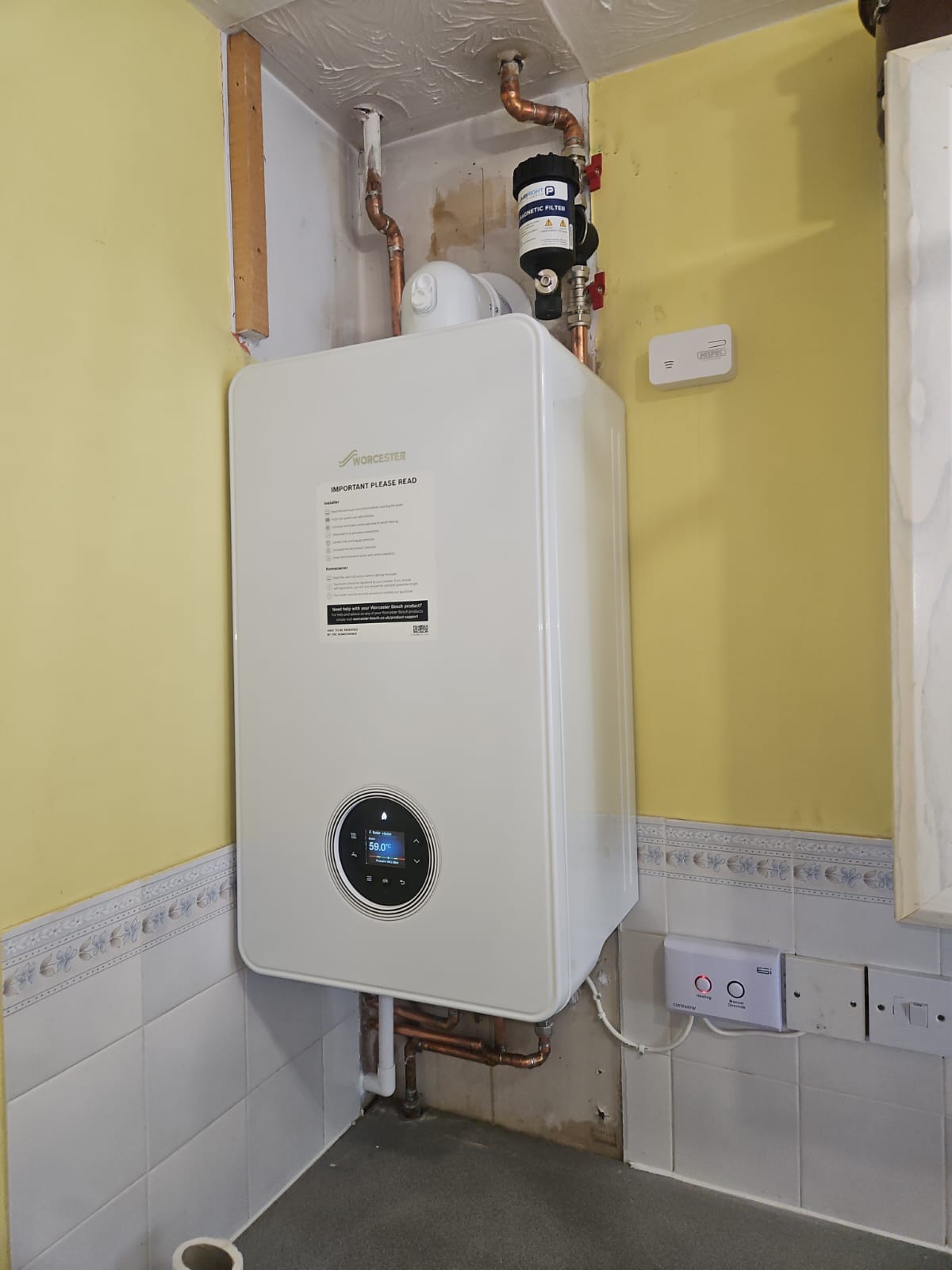boiler installation in Slough is shown, with a Worcester boiler mounted on a red brick wall. The digital display shows 24.8 degrees, and a notice is attached to the boiler's front panel.