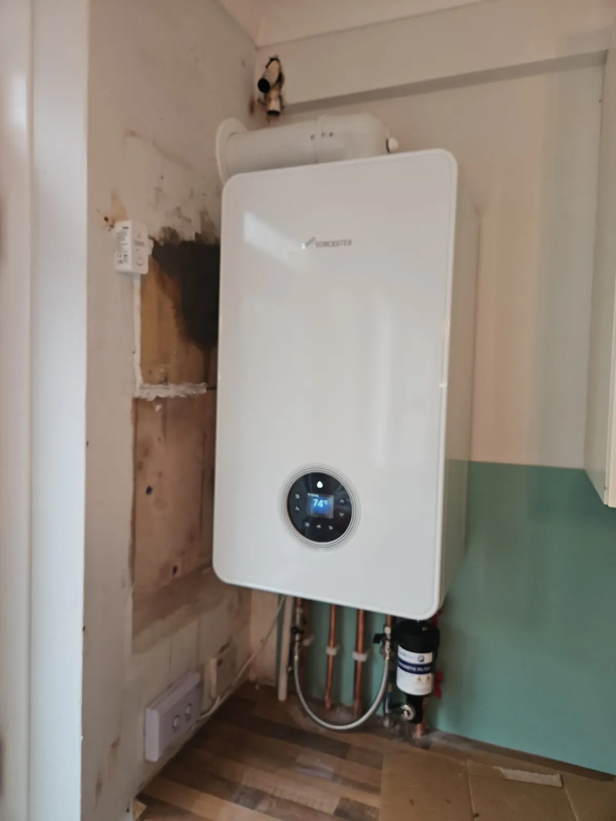 An image showing a new boiler installation in Slough, featuring a white Worcester boiler on a yellow wall with exposed copper pipes and a digital display showing a temperature of 58.9 degrees.